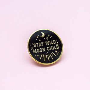 K&ouml;nnte beinhalten: Schwarzer Emaille-Pin mit goldener Aufschrift "Stay Wild Moon Child". Der Pin zeigt einen Halbmond und Sterne.