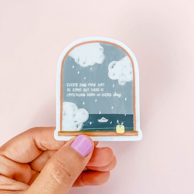 May include: A sticker with a window scene featuring a gray sky with white clouds, rain, and a small paper boat on the water. The text reads "EVERY DAY MAY NOT BE GOOD BUT THERE IS SOMETHING GOOD IN EVERY DAY."