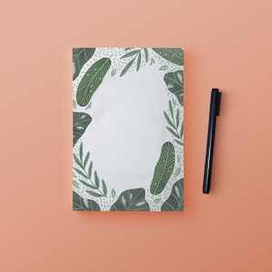 May include: A white notepad with a green and white floral border. The notepad is blank and ready to be written on.