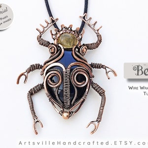 May include: A copper wire wrapped beetle pendant with a black stone and a yellow stone. The pendant is on a black cord and the text "Beetle Wire Wrapped Pendant Tutorial" is below the pendant.