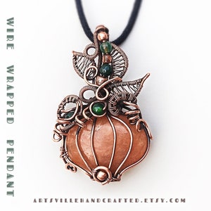 Pode incluir: Pingente envolto em fio de cobre em forma de abóbora com uma pedra cor de pêssego e detalhes verdes. O pingente está em um cordão preto.  "WIRE WRAPPED PENDANT PUMPKIN" e "TUTORIAL" estão escritos nos lados esquerdo e direito da imagem.  "ARTSVILLEHANDCRAFTED.ETSY.COM" está escrito na parte inferior da imagem.