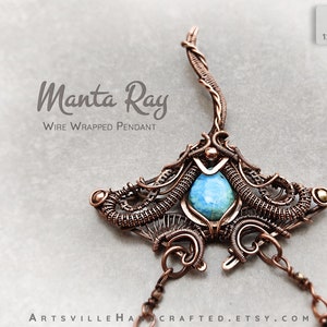 May include: A copper wire wrapped pendant in the shape of a manta ray with a blue gemstone in the center. The pendant is hanging from a chain. The text "Manta Ray Wire Wrapped Pendant" is visible in the image.