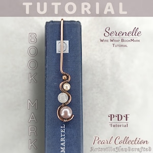 Op de afbeelding: Een koperdraad gewikkeld bladwijzer met een parel- en kralenontwerp, rustend op een blauw boek. De bladwijzer bevat de tekst "Serenelle WIRE WRAP BOOKMARK TUTORIAL" en "Pearl Collection ArtsvilleHandcrafted".