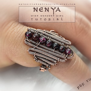 Puede incluir: Un anillo de alambre de cobre envuelto con un diseño geométrico y piedras preciosas rojas. El anillo está en un dedo y el texto "NENYA wire wrapped ring TUTORIAL PDF TUTORIAL" es visible.