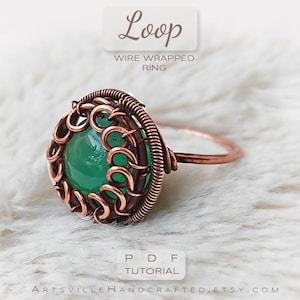 May include: A copper wire wrapped ring with a green gemstone. The ring is on a white fuzzy surface. The text "Loop Wire Wrapped Ring PDF Tutorial ArtsvilleHandcrafted.etsy.com" is at the bottom of the image.