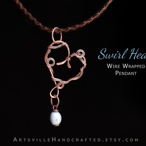 Pu&ograve; includere: Un ciondolo a forma di cuore avvolto in filo di rame con una perla bianca appesa alla parte inferiore. Il ciondolo &egrave; su un cordoncino di cuoio marrone. Il testo "Swirl Heart Wire Wrapped Pendant" &egrave; visualizzato sotto il ciondolo.