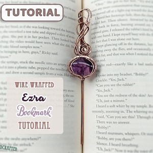 May include: A copper wire-wrapped bookmark with a purple gemstone and a long, slender stem. The bookmark is placed in an open book. The text on the bookmark says "Wire Wrapped Ezra Bookmark Tutorial".