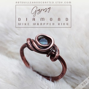 May include: A copper wire wrapped ring with a dark green gemstone. The ring is on a white fuzzy surface. The text "Gypsy Diamond Wire Wrapped Ring" is above the ring.