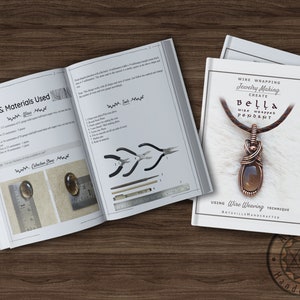 K&ouml;nnte beinhalten: Ein wei&szlig;es Heft mit dem Titel "Wire Wrapping Jewelry Making Create Bella Wire Wrapped Pendant Using Wire Weaving Technique ArtsvilleHandcrafted" und einem Bild eines mit Kupferdraht umwickelten Anh&auml;ngers mit einem braunen Edelstein. Das Heft liegt auf einer Holzoberfl&auml;che.