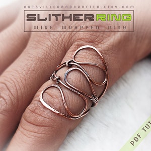 Op de afbeelding: Een ring van gewikkeld koperdraad met een uniek, organisch ontwerp. De ring wordt op een vinger getoond en is een statement piece. De afbeelding bevat ook de tekst "SLITHERRING WIRE WRAPPED RING" en "PDF TUTORIAL".