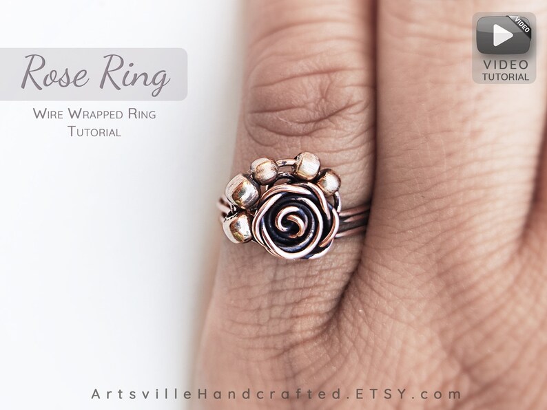 Pu&ograve; includere: Un anello avvolto in filo di rame con un design a forma di rosa. L'anello &egrave; indossato su un dito. La rosa &egrave; realizzata in filo di rame e ha un centro nero. L'anello &egrave; circondato da piccole perline di rame.
