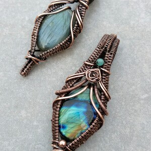 May include: Two copper wire wrapped pendants with labradorite gemstones. The top pendant has a green labradorite and the bottom pendant has a blue labradorite.