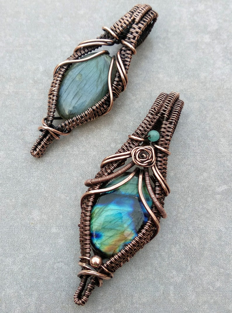 May include: Two copper wire wrapped pendants with labradorite gemstones. The top pendant has a green labradorite and the bottom pendant has a blue labradorite.