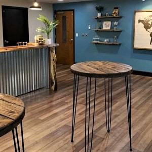 May include: Two round wooden tables with black hairpin legs. The tables are in a room with a blue wall and a wooden counter with a metal front.