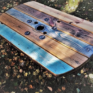 May include: A round wooden table made from repurposed cable spools. The table has a natural wood finish with blue and brown paint accents. The table has a hole in the center and is supported by black metal legs.