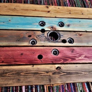May include: A wooden table top made from reclaimed wood with a circular hole in the center. The wood is stained in shades of brown, blue, red, and yellow.