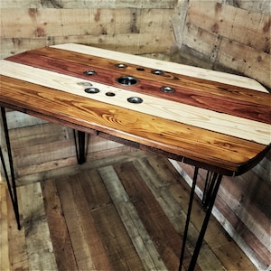May include: A rustic wooden table with a unique design featuring multiple circular cutouts. The table top is made of reclaimed wood with a multi-colored striped pattern. The table is supported by four black hairpin legs.