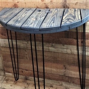 May include: A half-round wooden table with a dark gray stain and black hairpin legs. The table is made from reclaimed wood and has a rustic look.