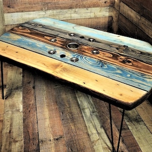 May include: A rustic wooden coffee table with a unique design. The table top is made from reclaimed wood with a blue, brown, and yellow color scheme. The table has a simple, industrial style with hairpin legs.
