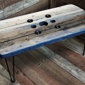 May include: A rustic wooden coffee table with a blue-stained top and black hairpin legs. The table top is made from reclaimed wood and has a unique design with five circular cutouts.