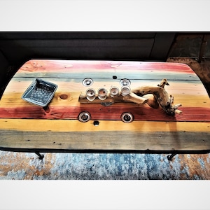 May include: A colorful wooden coffee table with a rustic driftwood centerpiece and a small gray ceramic dish. The table has a black metal frame and is decorated with six small glass candle holders.