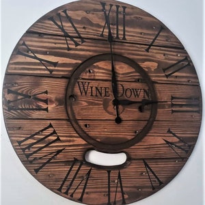 May include: A wooden clock with Roman numeral markings and the words "Wine Down" on the face. The clock is made from reclaimed wood and has a rustic, farmhouse style.