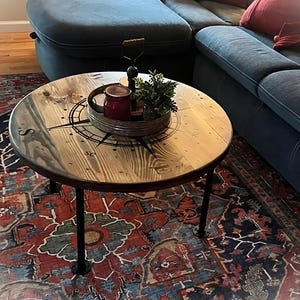 May include: A round wooden coffee table with a compass design and black metal legs. The table is sitting on a colorful rug.