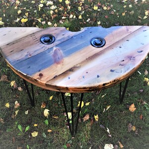 May include: A half-circle wooden table with a rustic, distressed finish. The table has two metal accents and is supported by three black hairpin legs.