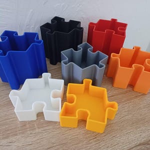 May include: A collection of colorful puzzle-shaped containers in blue, black, red, gray, orange, white, and yellow. These decorative containers are arranged on a wooden surface, showcasing their unique design and vibrant colors.