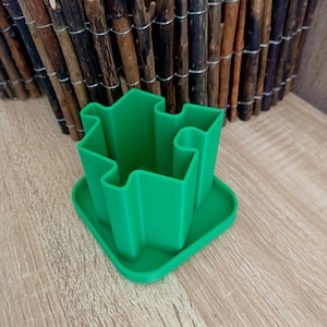 May include: A green plastic puzzle-shaped pencil holder with a square base.