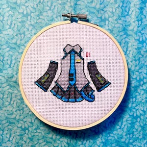 May include: Cross-stitch embroidery of a stylized anime outfit in a wooden hoop. The design features a gray jacket with a blue tie, blue accents, and black sleeves. The number "01" is visible in red.