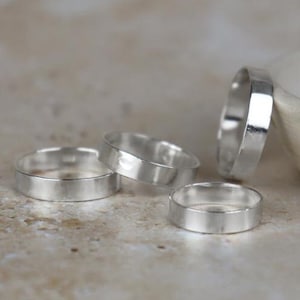 May include: Four silver rings of varying sizes, stacked on a light brown surface.