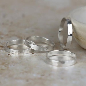 May include: Four silver hammered rings of varying sizes. The rings are stacked on a light brown surface.