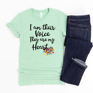 K&ouml;nnte beinhalten: Ein hellgr&uuml;nes T-Shirt mit dem Text "I am their Voice They are my Heart" und einem Herz aus Puzzle-Teilen in Rot, Blau, Gelb und Gr&uuml;n.