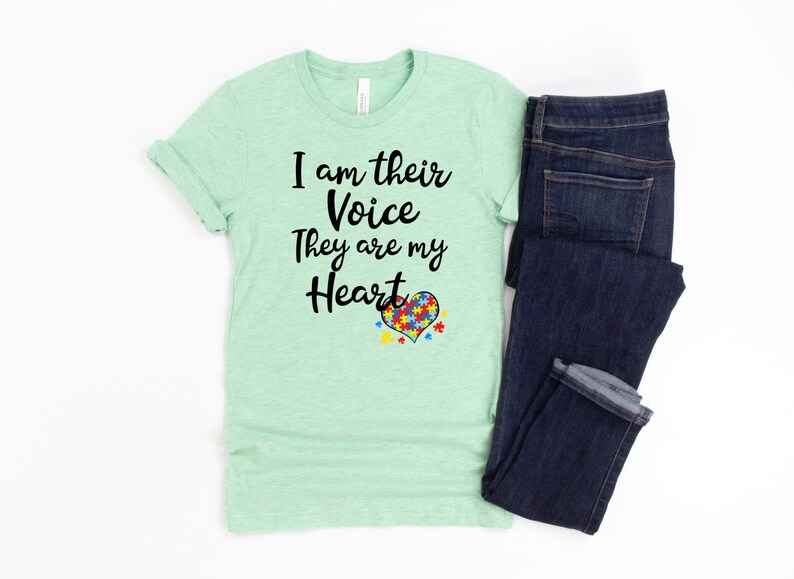 K&ouml;nnte beinhalten: Ein hellgr&uuml;nes T-Shirt mit dem Text "I am their Voice They are my Heart" und einem Herz aus Puzzle-Teilen in Rot, Blau, Gelb und Gr&uuml;n.