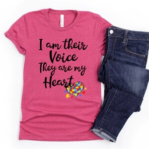 K&ouml;nnte beinhalten: Ein pinkfarbenes T-Shirt mit dem Text "I am their Voice They are my Heart" und einem Herz aus Puzzle-Teilen in Blau, Gelb, Gr&uuml;n und Rot.