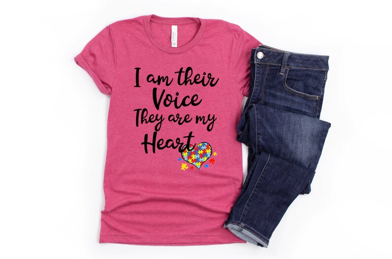 K&ouml;nnte beinhalten: Ein pinkfarbenes T-Shirt mit dem Text "I am their Voice They are my Heart" und einem Herz aus Puzzle-Teilen in Blau, Gelb, Gr&uuml;n und Rot.