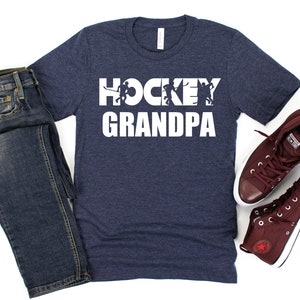May include: A navy blue t-shirt with the text "HOCKEY GRANDPA" in white. The text is made up of hockey players in silhouette.