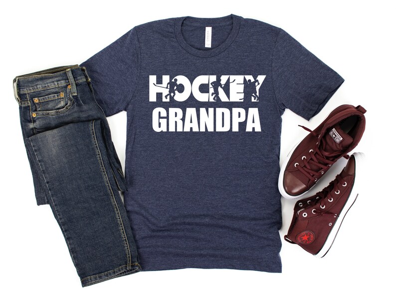 May include: A navy blue t-shirt with the text "HOCKEY GRANDPA" in white. The text is made up of hockey players in silhouette.