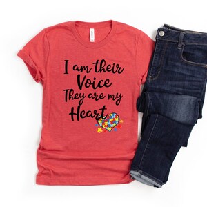 K&ouml;nnte beinhalten: Rotes T-Shirt mit dem Text "I am their Voice They are my Heart" und einem Herz aus Puzzle-Teilen in Blau, Gelb und Gr&uuml;n.