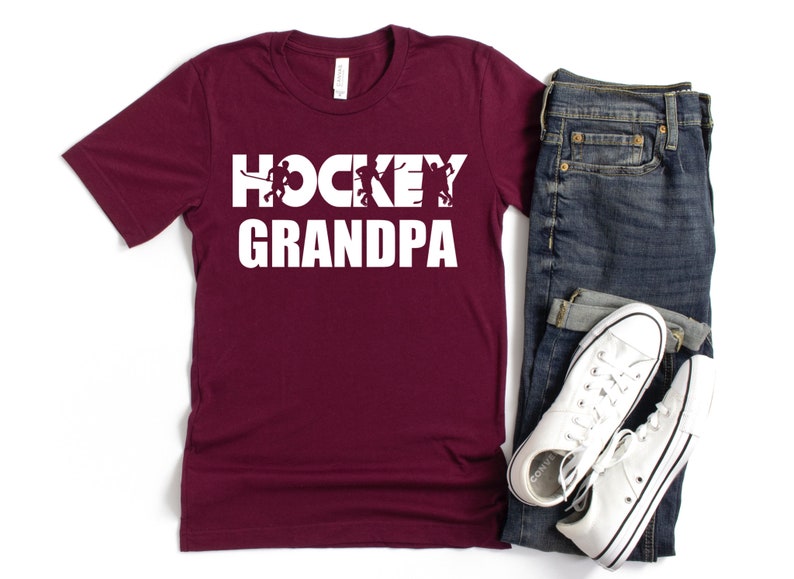 May include: Burgundy t-shirt with white text that reads "Hockey Grandpa" and features a silhouette of hockey players.