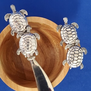 以下が含まれることがあります： 3つの亀の形をしたハンドルが付いた銀製のバターナイフ。ナイフは木製のボウルに入っています。亀は銀製で、細かな彫刻が施されています。