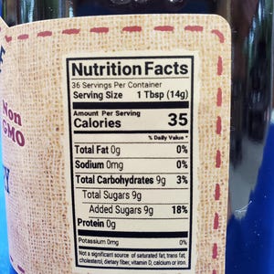 May include: Nutrition Facts label on a glass jar with a brown label. The label states 36 servings per container, 1 Tbsp (14g) per serving, 35 calories per serving, 0% daily value of total fat, 0% daily value of sodium, 3% daily value of total carbohydrates, 18% daily value of added sugars, and 0% daily value of potassium.