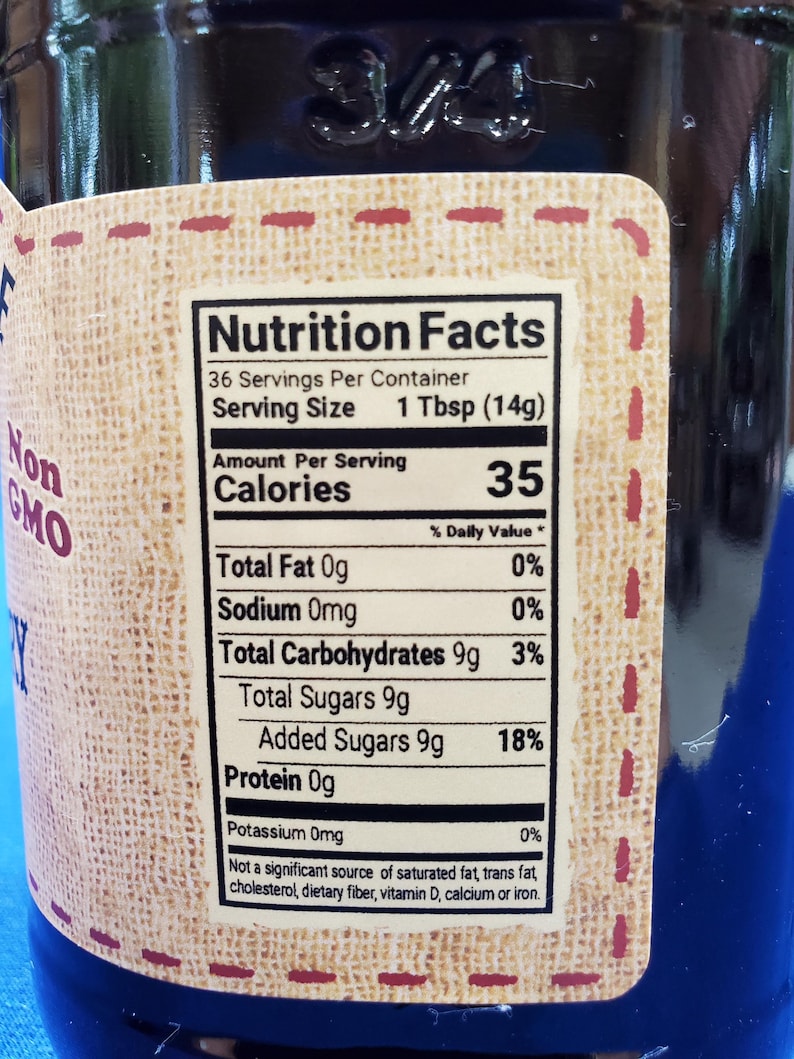 May include: Nutrition Facts label on a glass jar with a brown label. The label states 36 servings per container, 1 Tbsp (14g) per serving, 35 calories per serving, 0% daily value of total fat, 0% daily value of sodium, 3% daily value of total carbohydrates, 18% daily value of added sugars, and 0% daily value of potassium.