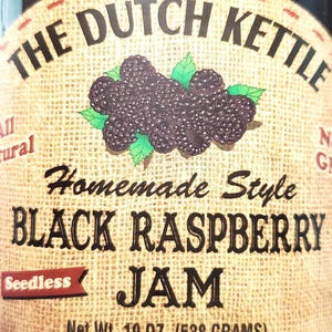 May include: A glass jar of The Dutch Kettle brand seedless black raspberry jam. The label features a burlap-textured background with an illustration of black raspberries and green leaves. The text reads: The Dutch Kettle, Homemade Style, Black Raspberry Jam, Seedless, Net Wt. 19 oz. (538 grams).