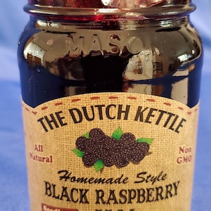 May include: A glass jar of The Dutch Kettle Homemade Style Black Raspberry Seedless Jam. The jar is filled with a dark red jam and has a brown label with the company name and product information. The label also states that the jam is all natural and non-GMO. The jar is 19 ounces (538 grams).