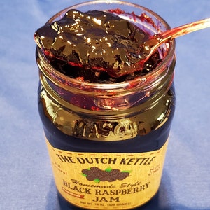 May include: A glass jar of homemade black raspberry jam with a gold label that reads "The Dutch Kettle Homemade Style Black Raspberry Jam" and "Net Wt. 18 oz (538 grams)".