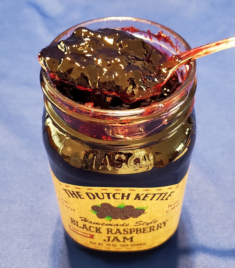 May include: A glass jar of homemade black raspberry jam with a gold label that reads "The Dutch Kettle Homemade Style Black Raspberry Jam" and "Net Wt. 18 oz (538 grams)".