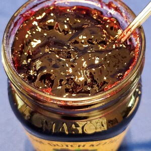 May include: A glass jar filled with dark red raspberry jam. The jar has a gold lid and a label that reads "The Dutch Kettle Black Raspberry Jam".