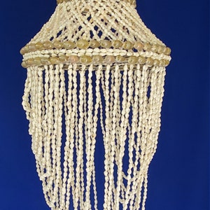 May include: A white shell chandelier with a brown shell top. The chandelier is made of many strands of shells that hang down from the top.